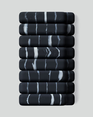 Nine black, rectangular objects with marble-like white streaks are stacked against a light gray background, with "BALA" faintly visible on the top. The design is modern and minimalist, showcasing the Vibrant Bangles Set for an Energizing Look.