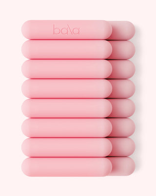 A set of ten cylindrical weights in light pink, embossed with "bala" on one, arranged in two columns against a soft off-white background for a sleek, modern vibe.