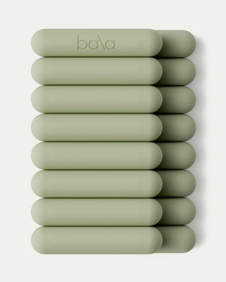 Ten sage green, cylindrical bangles from the Vibrant Bangles Set are arranged in two vertical stacks of five against a light gray background. One bangle in the top row features "bala" engraving, offering a modern, minimalist aesthetic reminiscent of fitness equipment.
