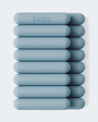 A neatly stacked grid of light blue oblong weights with rounded ends has three columns and five rows, topped with a "bala" logo. The background is pale blue, and they're named Vibrant Bangles Set for an Energizing Look.