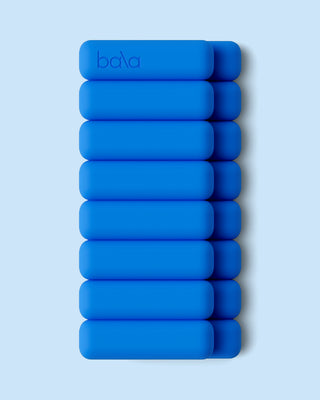 Nine bright blue, rounded rectangular items, branded with "bala" on the top one, are stacked in three rows against a light blue backdrop. The objects' even alignment casts subtle shadows rightward. Product: Vibrant Bangles Set for an Energizing Look.