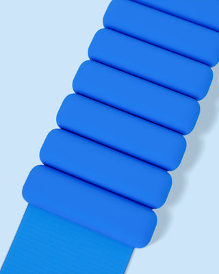 A close-up shot features a blue accordion-style strap, part of the Vibrant Bangles Set for an Energizing Look, against a light blue background. Rectangular segments overlap to create a flexible texture, with the smooth blue material providing contrast against the simple backdrop.