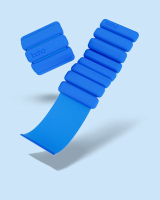 A pair of blue Vibrant Bangles Set wristbands on a light blue background. One is fully wrapped, the other partially unwrapped, showcasing its stretchy material. Both display "bala" in lowercase letters on a segment, casting shadows beneath.