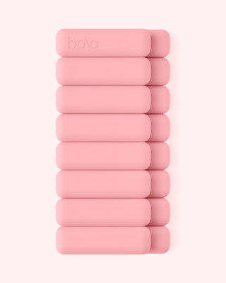 A stack of ten pink cylindrical weights with rounded edges, from the Vibrant Bangles Set for an Energizing Look, arranged vertically against a light pink background. The top weight displays the embossed "Bala" logo in a minimalist and symmetrical design.