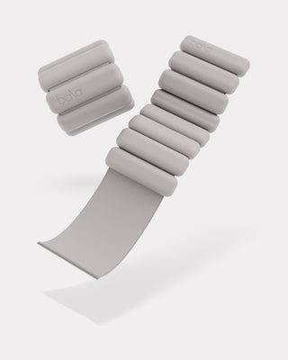 The image displays "Bala" embossed, gray adjustable wrist or ankle weights with a modern sleek design and soft cylindrical weights attached to a strap. The product, called the Vibrant Bangles Set for an Energizing Look, is pictured against a white background.