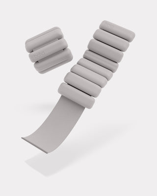 The Vibrant Bangles Set for an Energizing Look features gray wristbands with cylindrical weights; one is extended, displaying its elastic strap, and the other is rolled up. Each band boasts four smooth-finish weights on a white background.