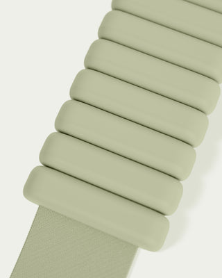 Close-up of diagonally arranged, connected pale green segments resembling a watch band from the Vibrant Bangles Set for an Energizing Look, with slightly overlapping parts and a fabric-like strap extending from the bottom left against an off-white background.