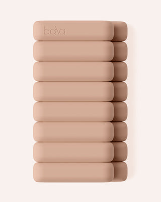 The Vibrant Bangles Set lies stacked vertically against a white background. Each beige, rectangular bangle is smooth, cushioned, and embossed with the brand name on the top piece. The uniform color and texture highlight its minimalist design.