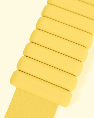 A close-up showcases a stack of Vibrant Bangles, smooth and glossy, arranged vertically on a light yellow background with a yellow strap partially visible beneath them.
