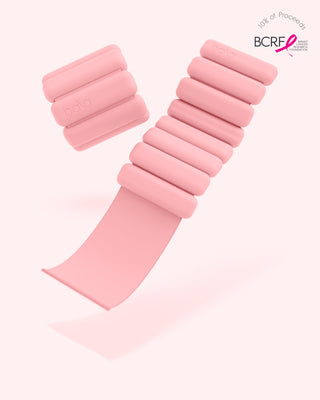 Displayed are vibrant bangles with rectangular segments, featuring an elastic strap and "bala" text. A "BCRF" logo with a pink ribbon indicates part of the proceeds support breast cancer research. The backdrop is soft pink.