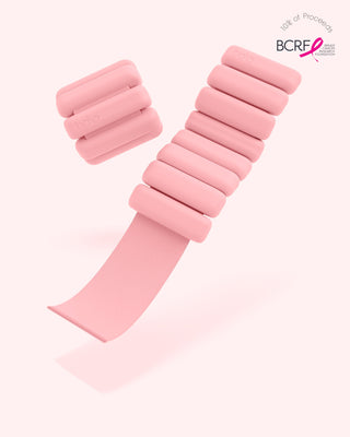 A pair of pink Vibrant Bangles Set for an Energizing Look wristbands with rectangular weights float on a white background. The top right corner shows text about 10% of proceeds benefiting the Breast Cancer Research Foundation, featuring a pink ribbon logo.