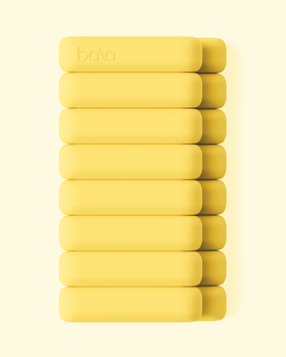 Nine yellow, rounded rectangular blocks embossed with "bala" are neatly stacked vertically against a cream background. Illuminated from the top left, they suggest movement in the Vibrant Bangles Set for an Energizing Look.