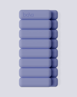 Nine lavender bars are stacked in staggered columns with a "Bala" debossed top bar. Set against a light gray background, they form the minimalist design of the Vibrant Bangles Set for an Energizing Look.