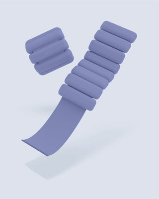 The Vibrant Bangles Set is displayed against a light gray background with two adjustable purple weighted bracelets having multiple cylindrical sections. One bracelet is fully assembled, the other partially open, revealing a gray strap. The weights subtly feature the "bala" brand name.