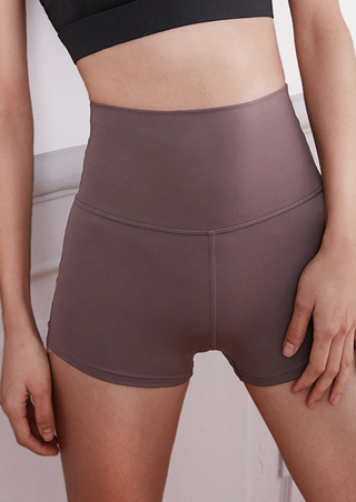 A person wears the Superflex Slinky Shorts in Milk Coffee and a black crop top, resting their hand casually beside them while standing in a relaxed pose against a minimal, neutral-toned background.