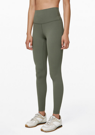 A person in High-Waist Powercore Leggings in Army Green and vintage-styled white sneakers with brown soles stands against a white background. With a snug fit and rounded toe design, the activewear is showcased as the person stands with arms down.