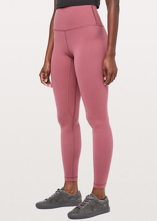 A person in Show Red High-Waist Powercore Leggings with side seams is paired with a black top and gray sneakers. Their arms rest at their sides against a plain white background.