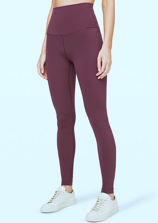 A person stands against a light blue background wearing High-Waist Powercore Leggings in dark red with white sneakers. The leggings are form-fitting and sporty, perfect for exercise. Only the lower half of the body is visible, with arms relaxed at their sides.