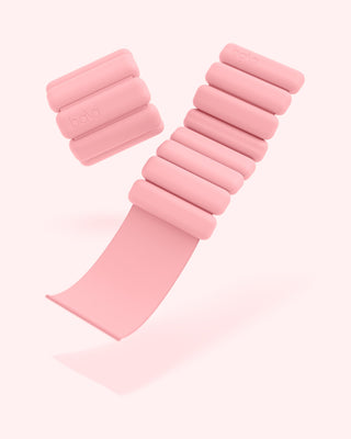 Adjustable pink wearable weights, embossed with "bala," feature cushioned, cylindrical segments. One is straight, and the other coiled. The Vibrant Bangles Set for an Energizing Look pairs perfectly against a light pink background.
