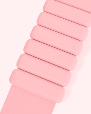 A close-up of a segmented watch band in vibrant pink shades lays against a light pink background. Rounded, rectangular links form this stunning bangle from the Vibrant Bangles Set for an Energizing Look, showcasing its smooth texture with perfectly matching strap.