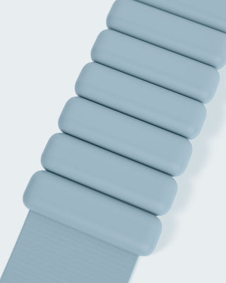 Close-up of the Vibrant Bangles Set, showcasing a light blue band with segmented links in a pill-shaped design. Seven horizontal links fade out of frame to the bottom left, all set against a pale blue background.