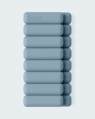 A minimalist image features ten teal cylindrical Vibrant Bangles stacked horizontally in two vertical rows against a light gray background, with the top left bangle displaying the "bala" logo.