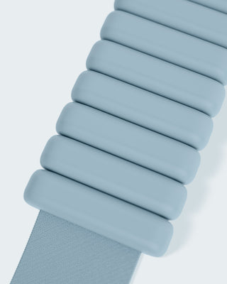 A close-up of a light blue accordion-style strap with rounded rectangular segments is aligned diagonally on a plain white background, highlighting the texture and design of the connected pieces from the Vibrant Bangles Set for an Energizing Look.