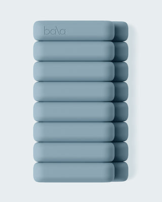 Ten light blue, rectangular Vibrant Bangles are stacked vertically against a light grey background. The rounded-edge bangles feature an embossed "bala" logo on the top one. The minimalist design emphasizes their smooth texture and uniform color.