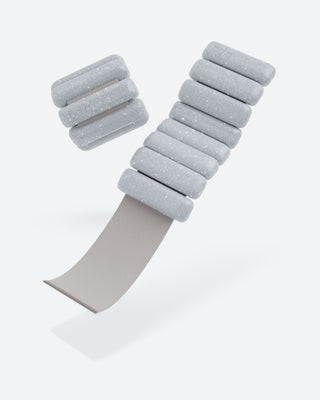 Minimalist image of the Vibrant Bangles Set for an Energizing Look featuring light gray, segmented foam-like pieces on a thin, curved band. Floating segments reveal textured surfaces with subtle dotted patterns, set against a plain white background.