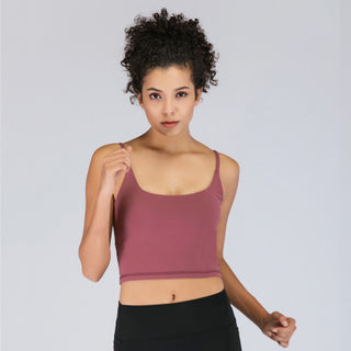 A person with curly hair is standing against a plain background. They are wearing the Cami Padded Sports Bra in a mauve color and black high-waisted leggings. The person's right arm is bent with their hand slightly raised, while the left arm is relaxed by their side.