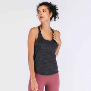 A woman with curly hair is posing against a plain background. She is wearing the dark grey sleeveless Tank Top + Bra and pink leggings. She has her right arm bent, with her hand touching her shoulder, while looking slightly to the side with a calm expression.