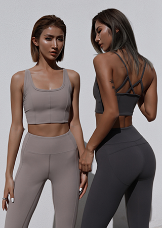 Two women are shown against a plain white background, modeling activewear. One faces forward, wearing a taupe sports bra and leggings, while the other faces away in the Meta Crisscross Padded Top in Coffee with matching leggings. Both outfits are fitted and stylish.